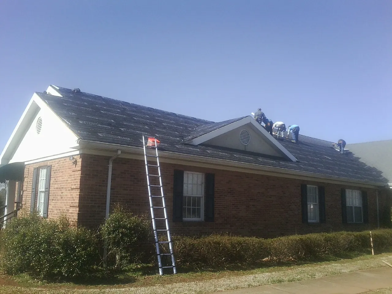 Crew tearing shingles off a brick ranch roof with a ladder set — Emergency Roof Repair work by our crew in Stevens Point