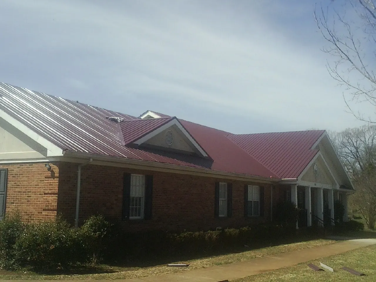 Red metal roof with gabled entries on a long brick building, from a Hail Damage Roof Repair job in Stevens Point