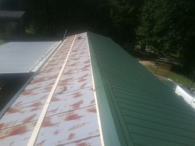 Old rusted panels beside newly installed green metal roofing — Wind Damage Roof Repair by Roofing Brothers in Stevens Point