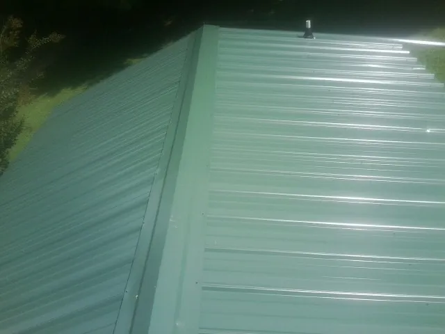 New green metal panels meeting at the ridge of a roof — Flat Roof Repair work by our crew in Stevens Point